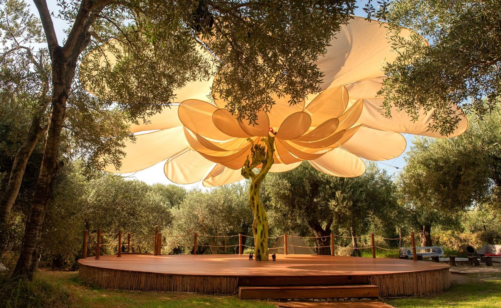 Wooden dance floor outdoors surrounded by trees with an orange fabric canopy above.